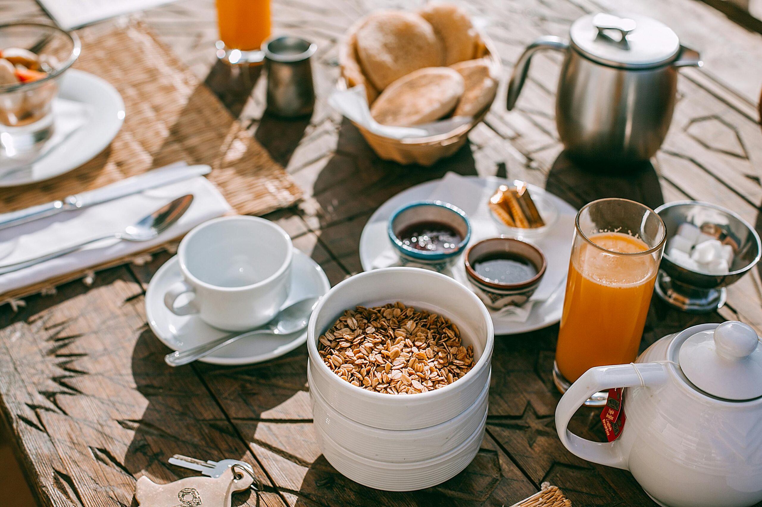An inviting breakfast setup with granola, tea, juice, and fresh bread on a rustic table.