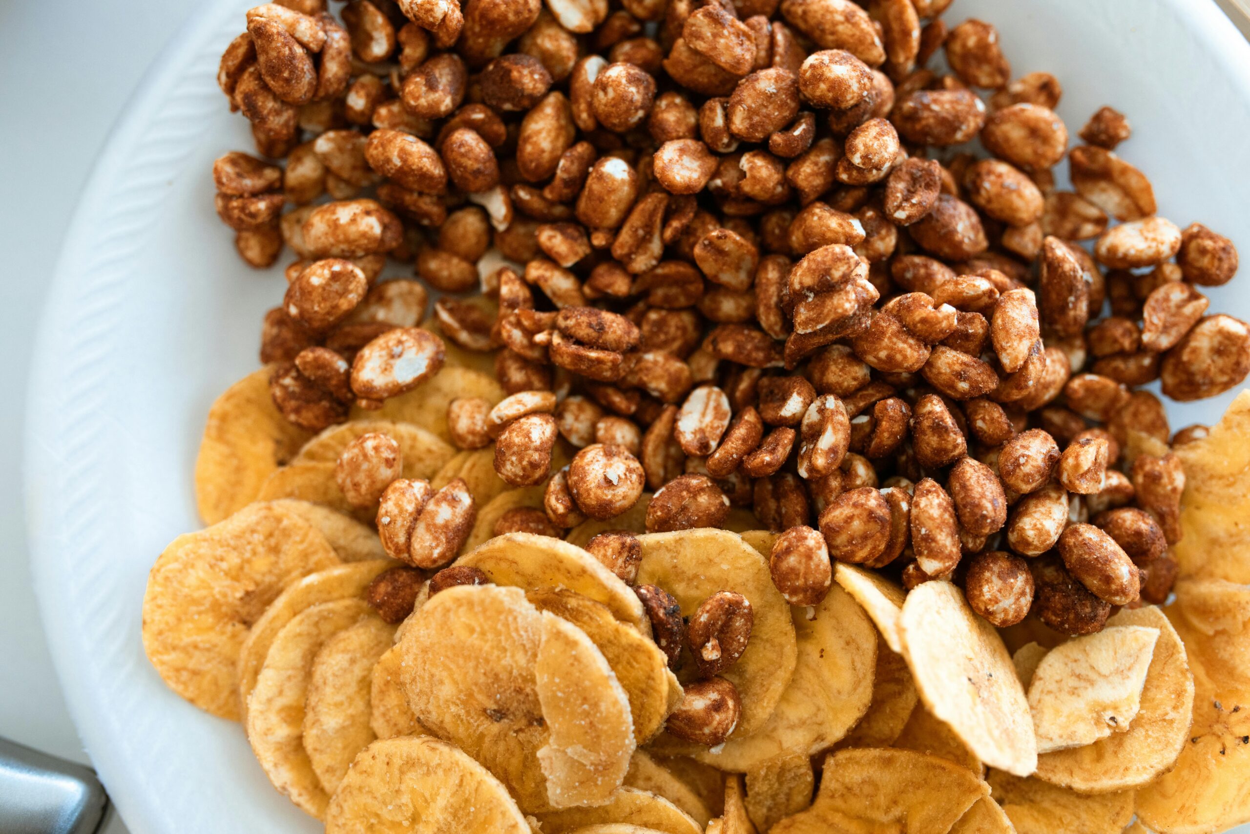 Close-up image of crispy banana chips and sweet honey roasted peanuts on a ceramic plate.